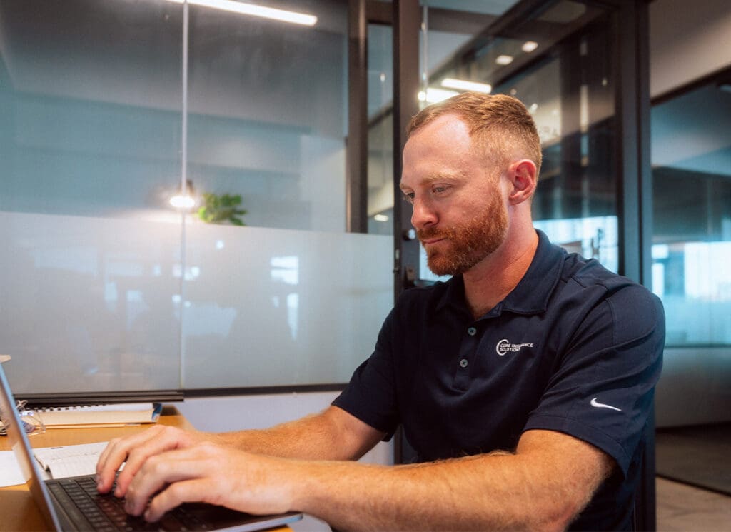 Homepage - About Core Insurance Solutions Working on Laptop at Desk in Office